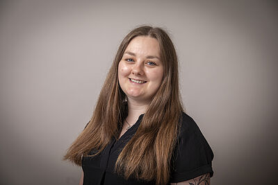 Op de foto zie je een vrouw van in de 20. Zij heeft lang bruin haar en staat lachend op de foto.